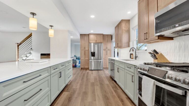 Modern kitchen with light green cabinets, stainless steel appliances, and wood floors.